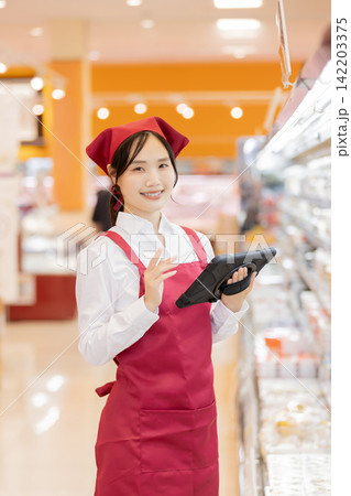 スーパーの商品棚でタブレットを使い在庫管理をする女性店員 スーパーの商品棚でタブレットを使い在庫管理をする女性店員 142203375