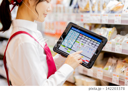 スーパーの商品棚でタブレットを使い商品発注をする女性店員 スーパーの商品棚でタブレットを使い商品発注をする女性店員 142203378