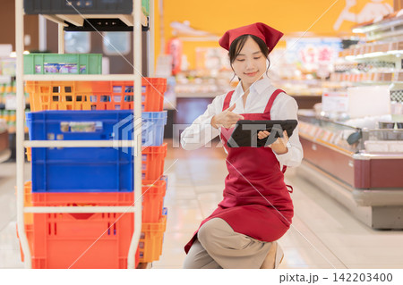スーパーでタブレットを持ち商品を確認する女性店員 スーパーでタブレットを持ち商品を確認する女性店員 142203400