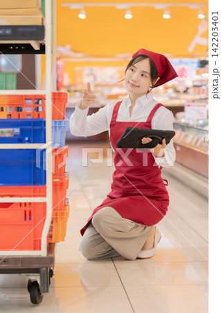 スーパーでタブレットを持ち商品を確認する女性店員 142203401