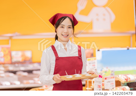 スーパーマーケットで試食をおすすめする笑顔の女性スタッフ スーパーマーケットで試食をおすすめする笑顔の女性スタッフ 142203479