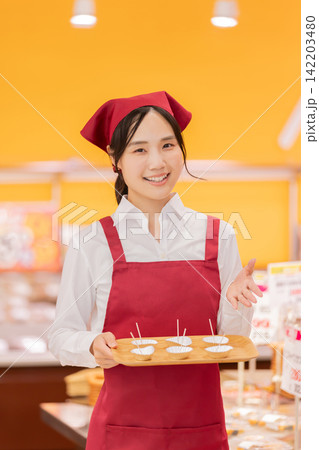 スーパーマーケットで試食をおすすめする笑顔の女性スタッフ 142203480