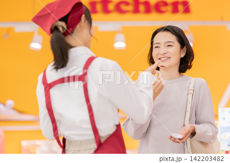 スーパーマーケットで試食を楽しむ笑顔の女性客と接客する女性スタッフ スーパーマーケットで試食を楽しむ笑顔の女性客と接客する女性スタッフ 142203482