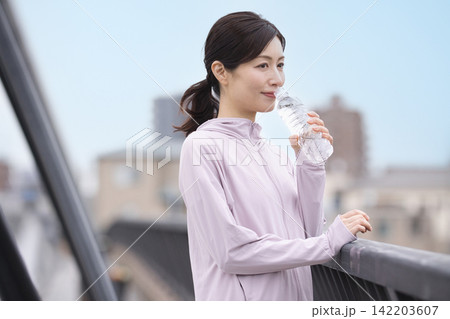 ウォーキング中にペットボトルの水を飲むミドル女性 ウォーキング中にペットボトルの水を飲むミドル女性 142203607