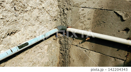 A PVC water pipe elbow fitting installed at the corner of a rough concrete wall. A PVC water pipe elbow fitting installed at the corner of a rough concrete wall. 142204343