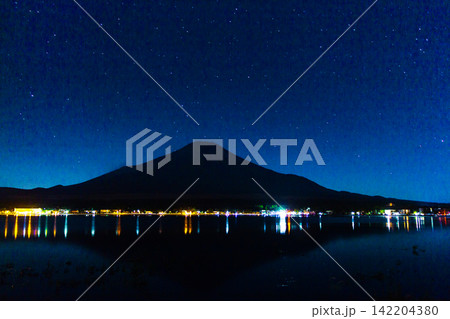 Mount Fuji Silhouette Under a Clear Deep Blue Starry Sky and Lake Lights Mount Fuji Silhouette Under a Clear Deep Blue Starry Sky and Lake Lights 142204380