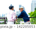 Two senior LGBTQ men share joyful moment on modern balcony with city skyline and lush greenery backdrop 142205053