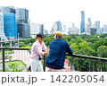 Two senior LGBTQ men share warm handshake on urban balcony overlooking lush green park and city skyline 142205054