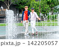 Two senior LGBTQ men walk joyfully through cascading fountain water in vibrant urban park 142205057