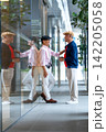 Two senior LGBTQ men laugh together beside glass wall, reflections mirror their joyful connection in urban setting 142205058