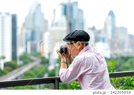 Senior LGBTQ man captures cityscape through vintage camera on modern balcony overlooking green park Senior LGBTQ man captures cityscape through vintage camera on modern balcony overlooking green park 142205059