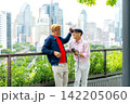 Senior LGBTQ men share affectionate moment on urban balcony with cityscape and vibrant greenery 142205060