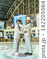 Two senior LGBTQ men in cream suits share tender moment at train station, one adjusting the other's cap with gentle hands. 142205064