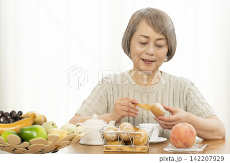 リビングで朝食のパンを食べるシニア女性 リビングで朝食のパンを食べるシニア女性 142207929