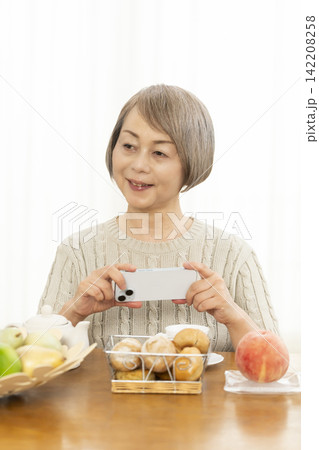 リビングでスマホ操作しながら朝食のパンを食べるシニア女性 142208258