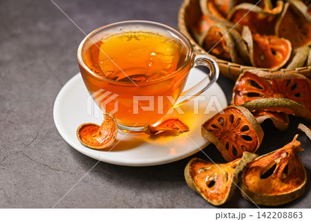 Bael tea on glass with dried bael slices on dark background, Bael juice - Dry bael fruit tea for health - Aegle marmelos Bael tea on glass with dried bael slices on dark background, Bael juice - Dry bael fruit tea for health - Aegle marmelos 142208863