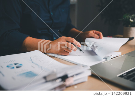Business professional reviewing printed financial reports with charts beside a laptop, representing data analysis, accounting, auditing, business performance, and strategic decision making. 142209921