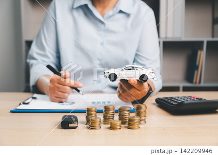 Financial advisor holding a white toy car with stacks of coins on desk, symbolizing car loan approval, vehicle financing, budget planning, savings, and automobile ownership concept. Financial advisor holding a white toy car with stacks of coins on desk, symbolizing car loan approval, vehicle financing, budget planning, savings, and automobile ownership concept. 142209946