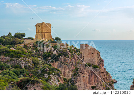 Ancient watchtower perched on a rocky cliff overlooking the blue sea Ancient watchtower perched on a rocky cliff overlooking the blue sea 142210036