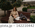 Mom sits on a bench while daughter lays on her lap in a park during daytime 142210442