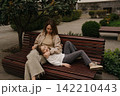 The mother sits on a bench in the garden, her daughter lies on her lap enjoying the time spent together. 142210443