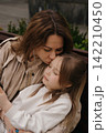 Mom kisses her little daughter while sitting on a bench in the park in the afternoon sun 142210450