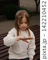 Little girl observes a ladybug on her hand while sitting on a bench outdoors in the park 142210452