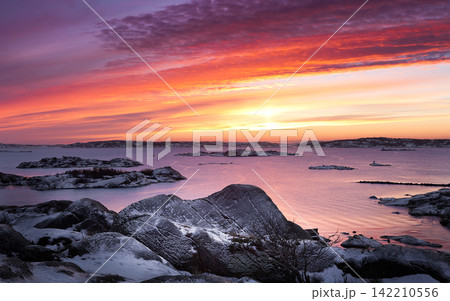 Winter Coastal Sunset Over Snowy Rocky Islands and Calm Sea Winter Coastal Sunset Over Snowy Rocky Islands and Calm Sea 142210556
