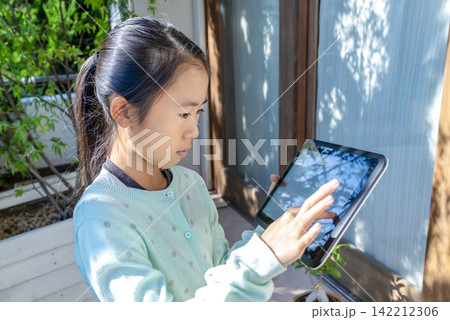 自宅のベランダでタブレットを操作する小学生の女の子 142212306