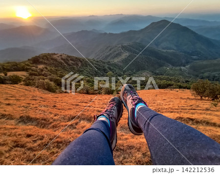 Legs traveler woman and trekking shoes relaxing and hanging on cliff with dry grass and golden sunlight on mountain peak scene in Thailand Legs traveler woman and trekking shoes relaxing and hanging on cliff with dry grass and golden sunlight on mountain peak scene in Thailand 142212536