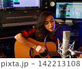 Young female singer with acoustic guitar recording a song promo in a studio 142213108