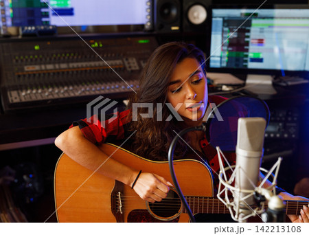 Young female singer with acoustic guitar recording a song promo in a studio 142213108