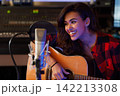 Woman singer in studio. Young artist with guitar recording her song. 142213308