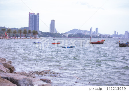 Fishing boats and waves crashing against the rocky shore 142213939