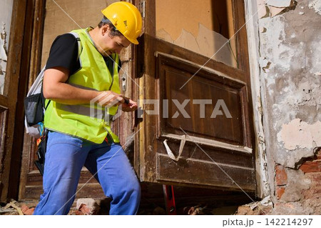 Worker inspects doorway measurements in deteriorating building 142214297