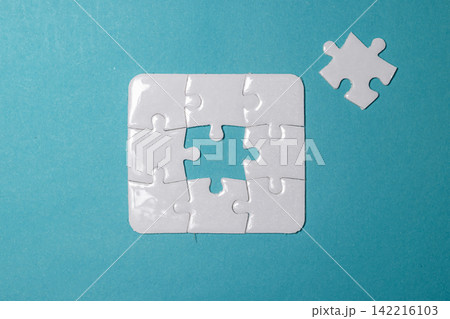 White jigsaw puzzle missing its center piece with the final piece placed nearby on a blue background. High Quality Photo 142216103