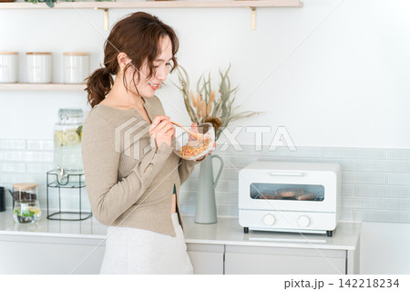 キッチンで手軽にグラノーラで朝食を取るアジア人女性 キッチンで手軽にグラノーラで朝食を取るアジア人女性 142218234