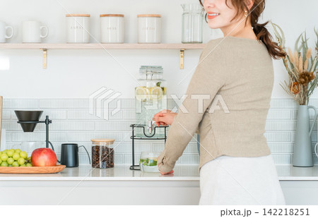 キッチンカウンターでウォーターサーバーからデトックスウォーターを注ぐ女性 142218251