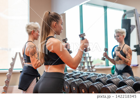Two women lifting heavy dumbbells during workout in modern fitness gym 142218345