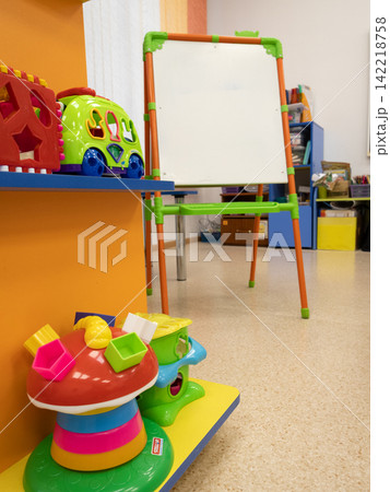 Green ride-on toy bus with blue wheels in an indoor playroom among colorful blocks and a whiteboard 142218758