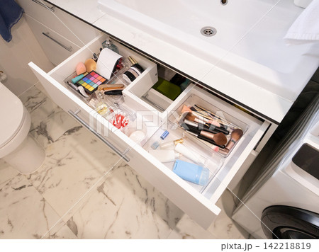 Open bathroom vanity drawer displaying neatly organized makeup tools in a modern marble setting Open bathroom vanity drawer displaying neatly organized makeup tools in a modern marble setting 142218819