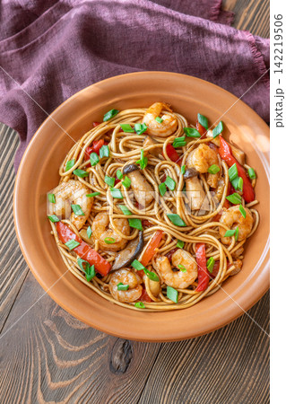 Asian stir fry udon noodles with prawns mushrooms vegetables in rustic ceramic bowl Asian stir fry udon noodles with prawns mushrooms vegetables in rustic ceramic bowl 142219506