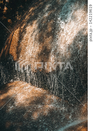 Closeup of water flowing over textured rock surface creating natural abstract pattern and motion, Minimal cascade detail with wet stone and dynamic water splash in tropical environment Closeup of water flowing over textured rock surface creating natural abstract pattern and motion, Minimal cascade detail with wet stone and dynamic water splash in tropical environment 142219619