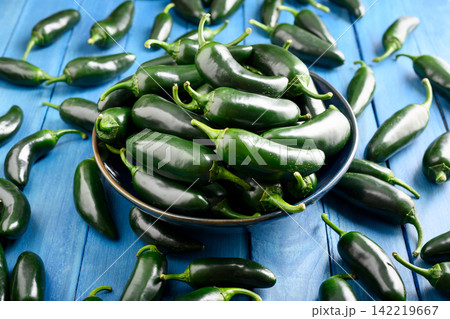 Flat lay scattered jalapeno peppers with bowl on blue wooden background Flat lay scattered jalapeno peppers with bowl on blue wooden background 142219667