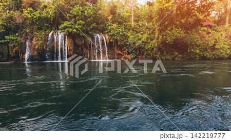 Sai Yok Yai waterfall in Thailand flowing into river surrounded by lush tropical jungle in national park, Wide scenic cascade with rich textures and natural beauty, travel and tranquility Sai Yok Yai waterfall in Thailand flowing into river surrounded by lush tropical jungle in national park, Wide scenic cascade with rich textures and natural beauty, travel and tranquility 142219777