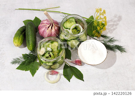 Cucumbers with dill, garlic, horseradish, pickling leaves, and pickled cucumbers in jars on the kitchen counter. Harvest concept. Recipe and ingredients for homemade pickles. Concept of home canning Cucumbers with dill, garlic, horseradish, pickling leaves, and pickled cucumbers in jars on the kitchen counter. Harvest concept. Recipe and ingredients for homemade pickles. Concept of home canning 142220126