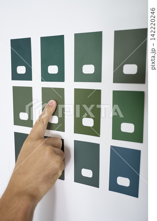 Hand points to one of several green paint color samples on white wall Hand points to one of several green paint color samples on white wall 142220246