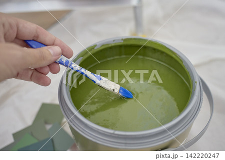 Hand mixes green paint with small brush in open paint can Hand mixes green paint with small brush in open paint can 142220247