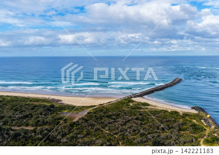 Aerial view of North Shore Beach and the breakwall surrounded by the Pacific Ocean, showcasing the sandy shoreline, coastal waters and river entrance near Port Macquarie on the Mid North Coast of NSW Aerial view of North Shore Beach and the breakwall surrounded by the Pacific Ocean, showcasing the sandy shoreline, coastal waters and river entrance near Port Macquarie on the Mid North Coast of NSW 142221183