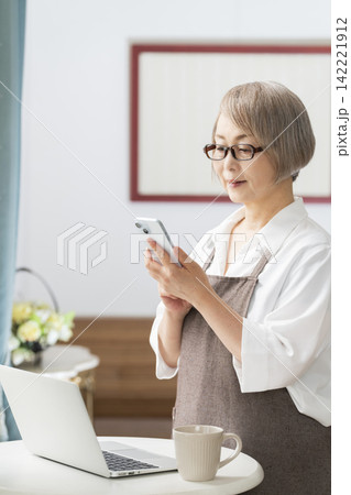 リビングの窓辺でノートパソコンを使うシニア女性 リビングの窓辺でノートパソコンを使うシニア女性 142221912